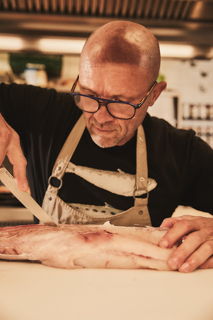 Rainer Trautenbach lehnt sich über ein Fisch- oder Fleischstück auf dem Arbeitstisch