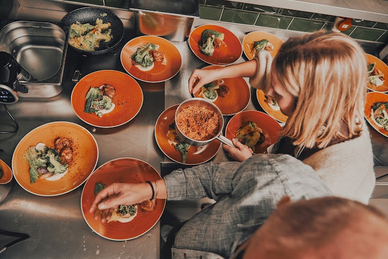 Kochkursteilnehmerin richtet orange Teller mit Gemüse und Fleisch an