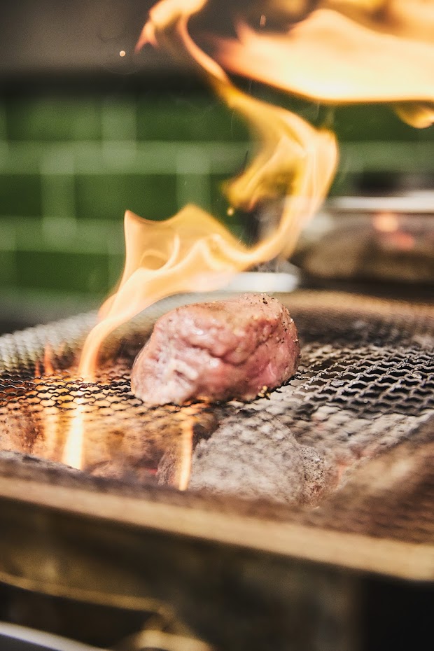 Fleisch auf dem Grill mit offenem Feuer – dramatischer Kochmoment in der Profiküche