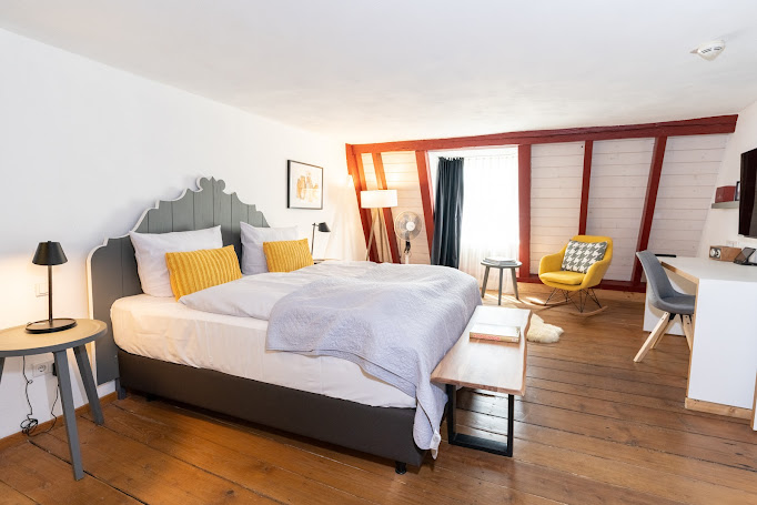 Helles Fachwerkzimmer mit Doppelbett und gelbem Schaukelstuhl